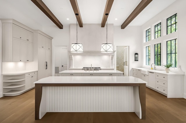 kitchen with wood-type flooring, white cabinetry, hanging light fixtures, beam ceiling, and a spacious island