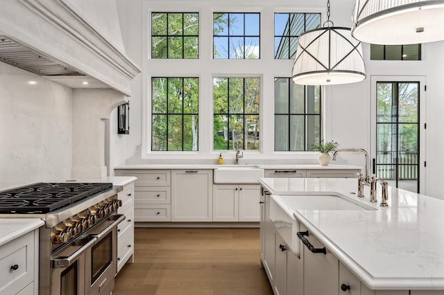 kitchen featuring sink, hanging light fixtures, double oven range, an island with sink, and white cabinets