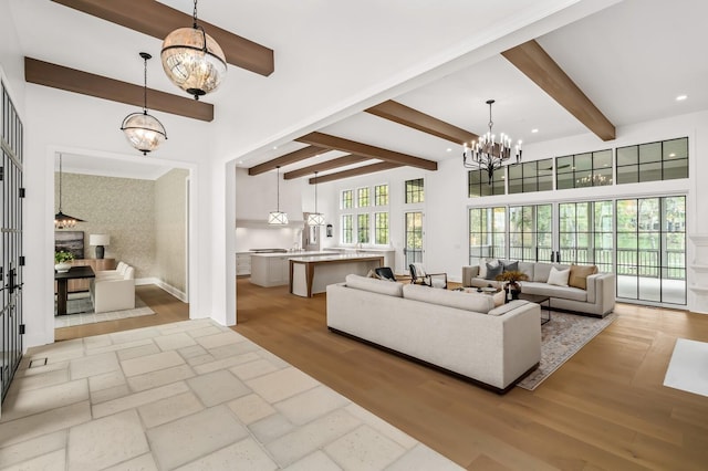 living room with beam ceiling, light hardwood / wood-style flooring, a chandelier, and a towering ceiling