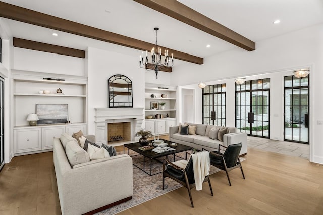 living room featuring beam ceiling, a notable chandelier, light hardwood / wood-style floors, and built in shelves