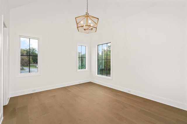 unfurnished room featuring wood-type flooring, plenty of natural light, a towering ceiling, and an inviting chandelier