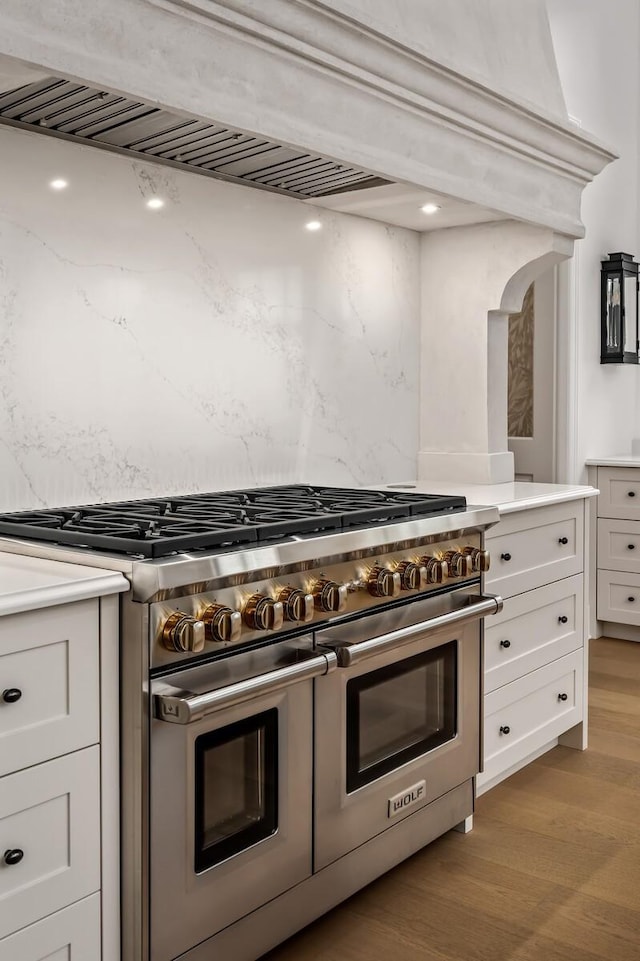 kitchen with light hardwood / wood-style flooring, double oven range, light stone counters, white cabinets, and custom exhaust hood