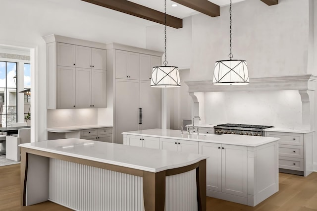 kitchen featuring sink, decorative light fixtures, beamed ceiling, and a large island with sink