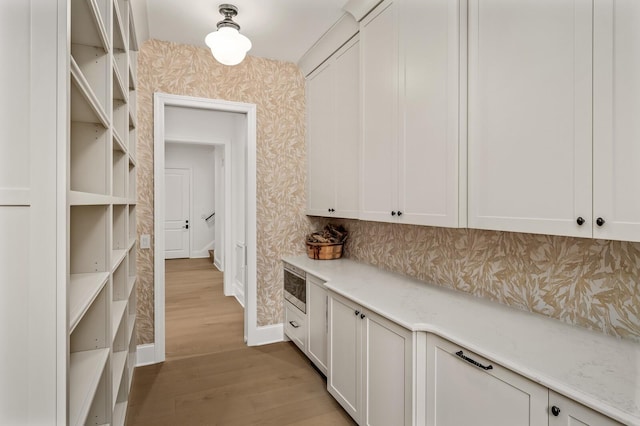 interior space with light stone counters, stainless steel microwave, light hardwood / wood-style floors, and white cabinets