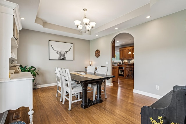 dining room with an inviting chandelier, light hardwood / wood-style floors, and a raised ceiling