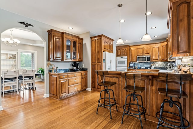 kitchen featuring sink, white appliances, a breakfast bar area, tasteful backsplash, and light hardwood / wood-style floors