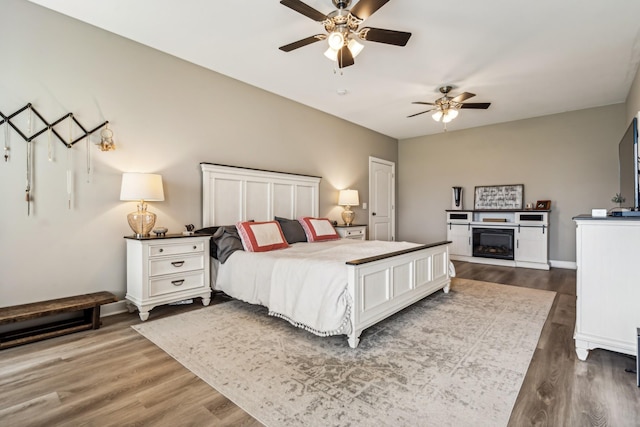 bedroom featuring dark wood-type flooring, ceiling fan, and a fireplace