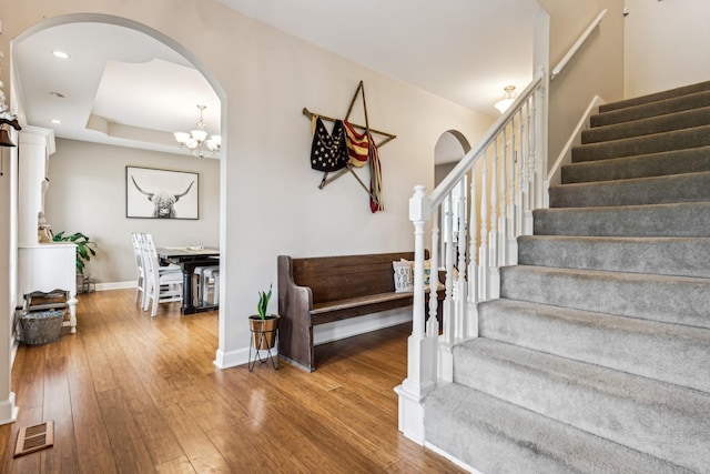 stairs featuring hardwood / wood-style flooring, a tray ceiling, and an inviting chandelier