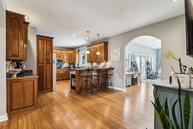 kitchen with tasteful backsplash, decorative light fixtures, fridge, a kitchen breakfast bar, and light hardwood / wood-style floors