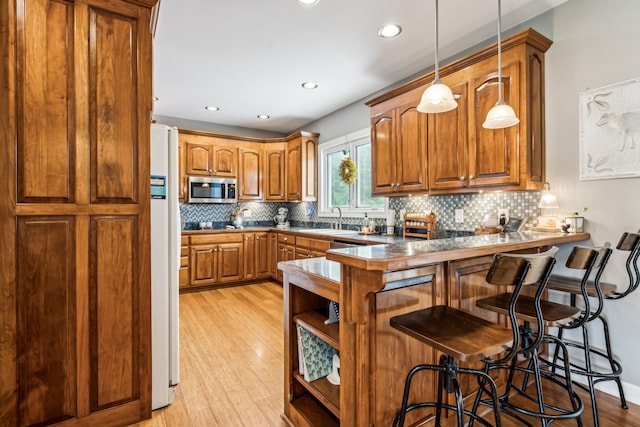 kitchen featuring sink, decorative light fixtures, a kitchen breakfast bar, kitchen peninsula, and light hardwood / wood-style floors