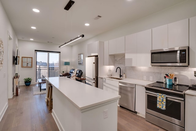 kitchen featuring sink, white cabinets, pendant lighting, stainless steel appliances, and backsplash