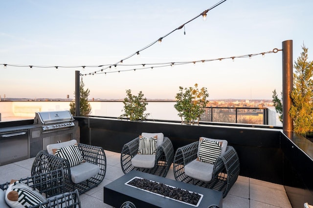 patio terrace at dusk with exterior kitchen, a water view, area for grilling, and a fire pit