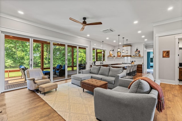 living room featuring ceiling fan, ornamental molding, sink, and light hardwood / wood-style floors