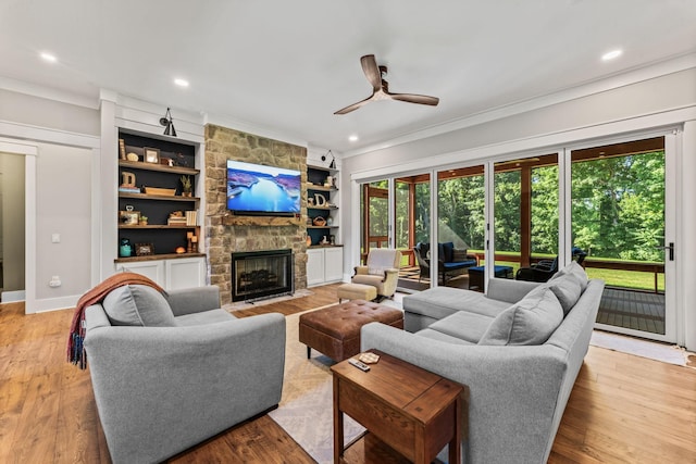 living room featuring built in shelves, light wood-type flooring, ornamental molding, ceiling fan, and a fireplace