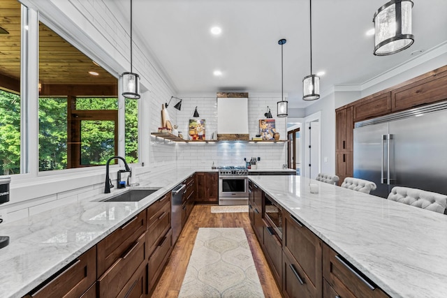 kitchen with decorative light fixtures, sink, decorative backsplash, built in appliances, and light stone counters