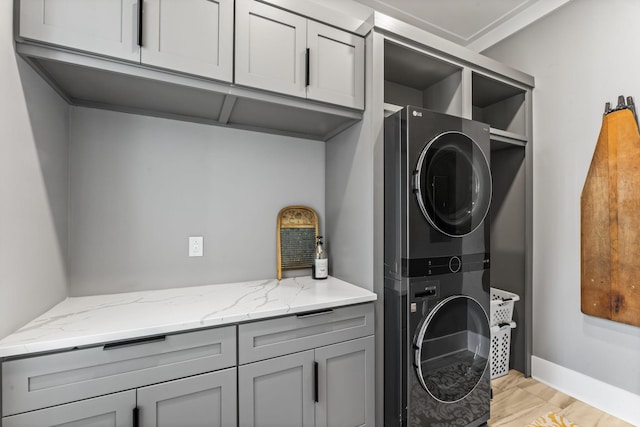 laundry area featuring cabinets, stacked washer / drying machine, and light wood-type flooring