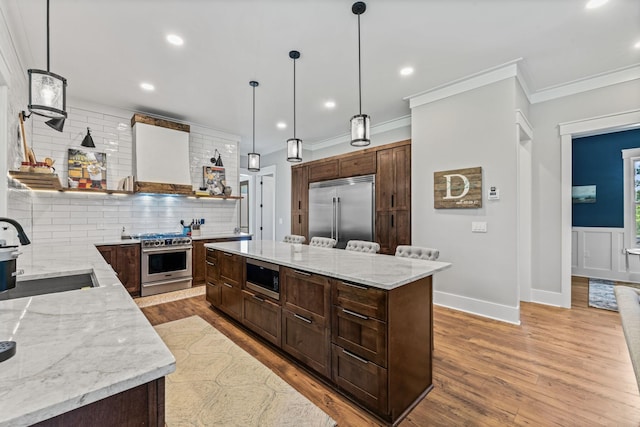 kitchen with sink, light stone counters, built in appliances, a kitchen island, and pendant lighting