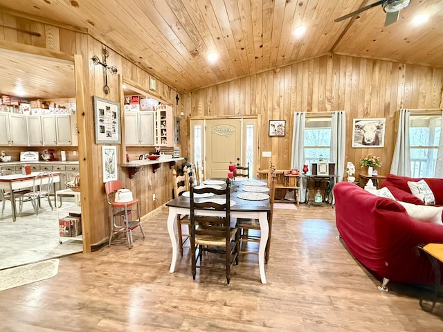 dining space with wooden walls, a ceiling fan, lofted ceiling, wood ceiling, and light wood-type flooring