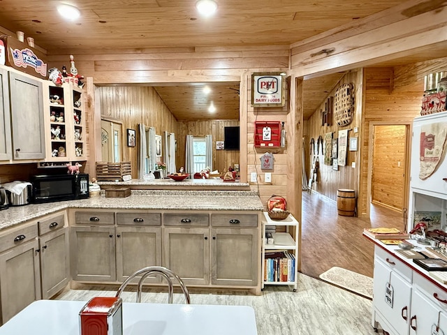 kitchen with wood ceiling, black microwave, light countertops, and wood walls