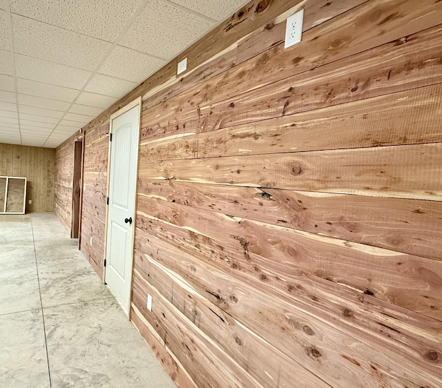 hall featuring wood walls and a paneled ceiling