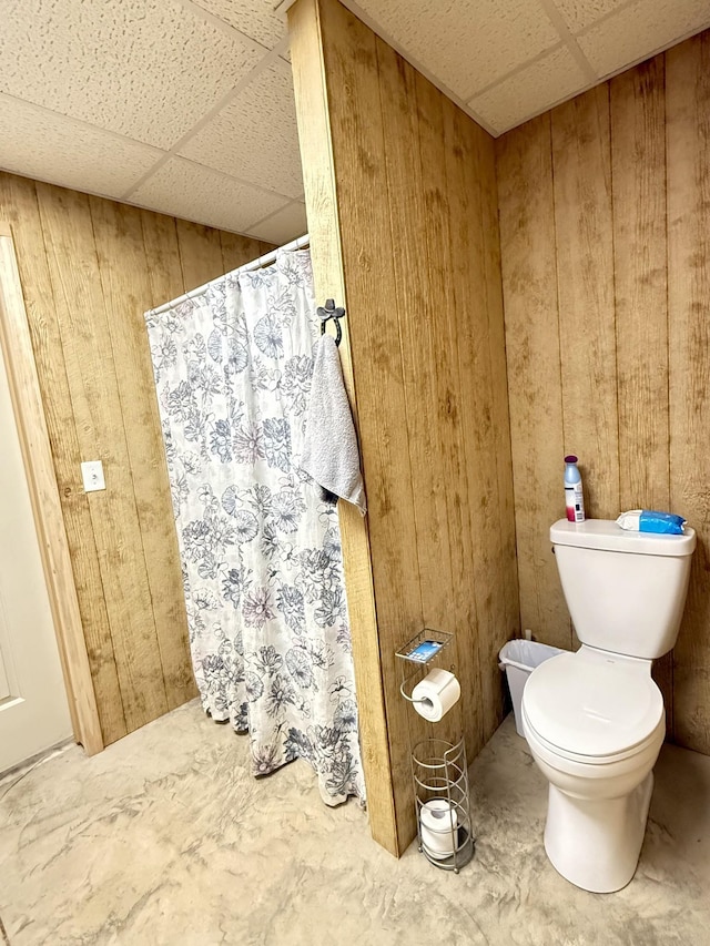 bathroom featuring a paneled ceiling, wooden walls, and toilet