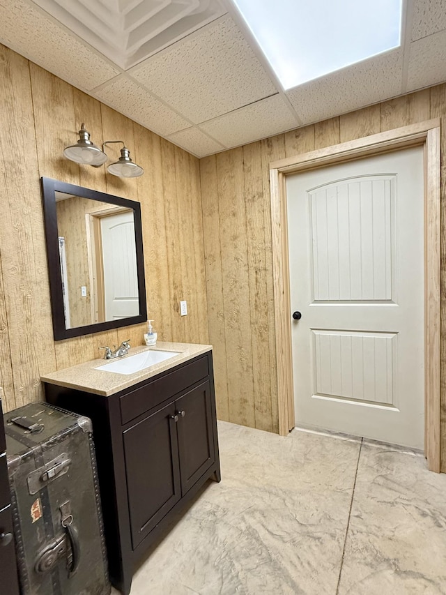 bathroom with a paneled ceiling, wood walls, and vanity