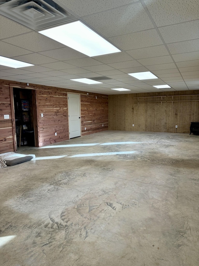 empty room with visible vents, concrete floors, wooden walls, and a drop ceiling