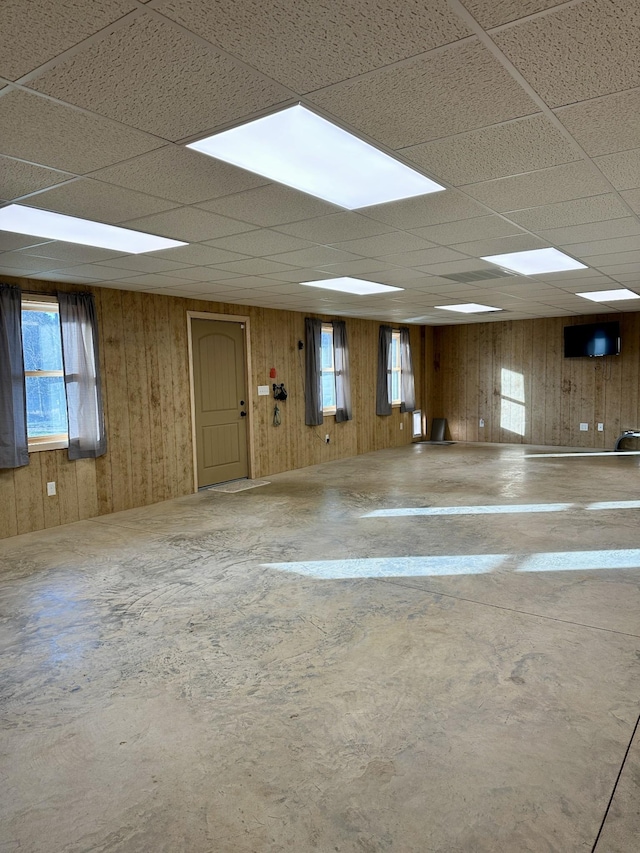 spare room featuring wood walls, concrete floors, and a drop ceiling