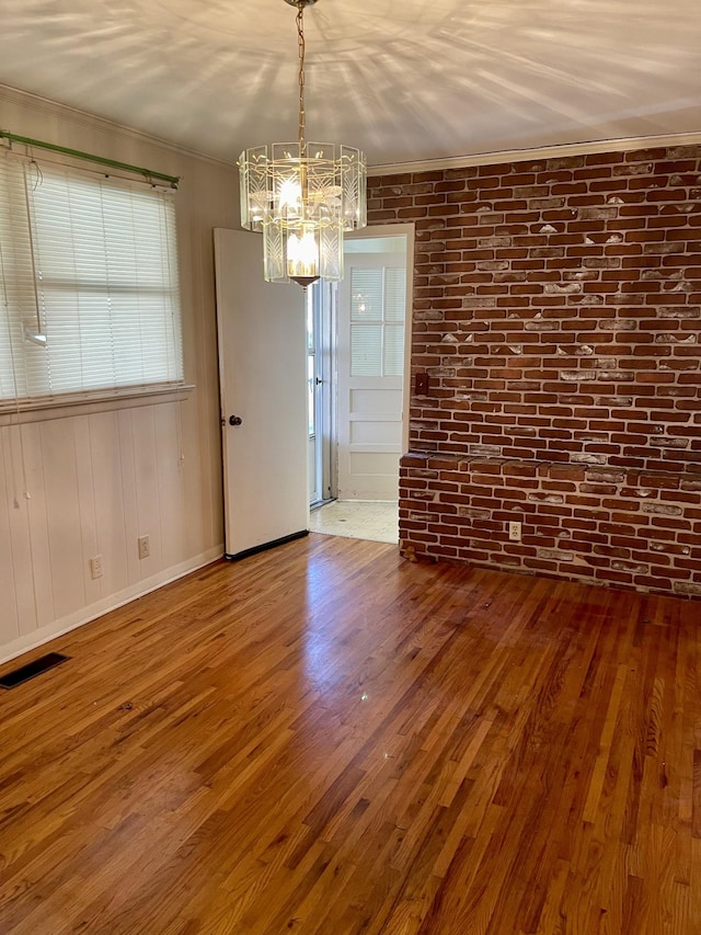 unfurnished dining area featuring hardwood / wood-style flooring, crown molding, brick wall, and an inviting chandelier