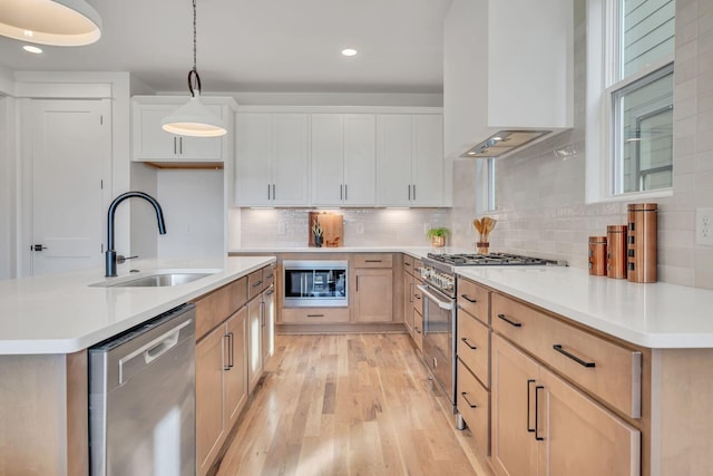 kitchen with pendant lighting, sink, light hardwood / wood-style flooring, range hood, and stainless steel appliances