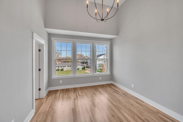 unfurnished dining area featuring an inviting chandelier, light hardwood / wood-style flooring, and a high ceiling