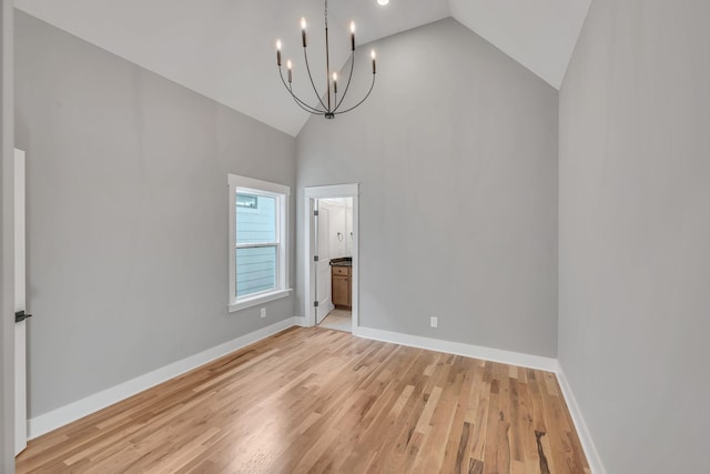 spare room with high vaulted ceiling, an inviting chandelier, and light hardwood / wood-style floors