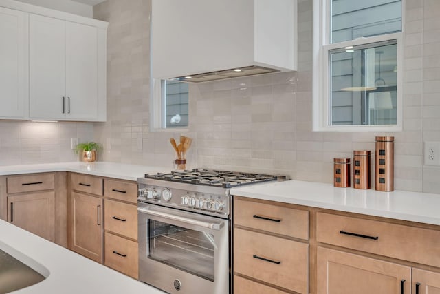 kitchen featuring premium range hood, tasteful backsplash, white cabinets, stainless steel range, and light brown cabinets