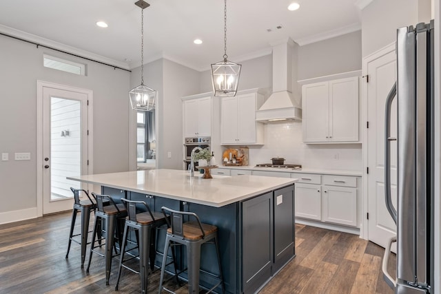 kitchen featuring stainless steel appliances, an island with sink, white cabinetry, and decorative light fixtures