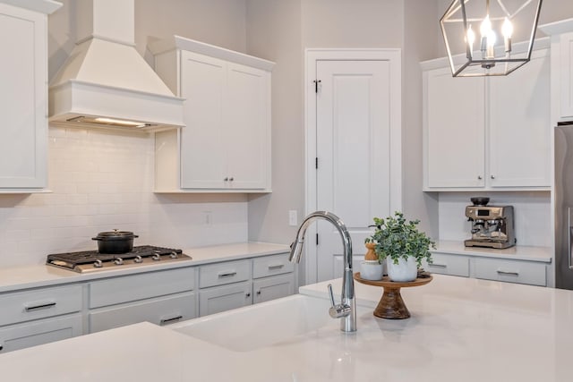 kitchen with appliances with stainless steel finishes, decorative light fixtures, white cabinetry, sink, and custom exhaust hood