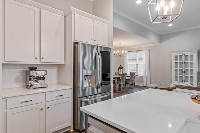 kitchen featuring stainless steel refrigerator with ice dispenser, crown molding, white cabinets, a notable chandelier, and backsplash