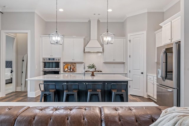 kitchen featuring pendant lighting, appliances with stainless steel finishes, a kitchen island with sink, and custom exhaust hood