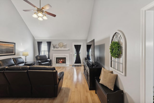 living room featuring a premium fireplace, high vaulted ceiling, ceiling fan, and light wood-type flooring