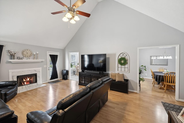 living room featuring a high end fireplace, light hardwood / wood-style flooring, high vaulted ceiling, and ceiling fan with notable chandelier