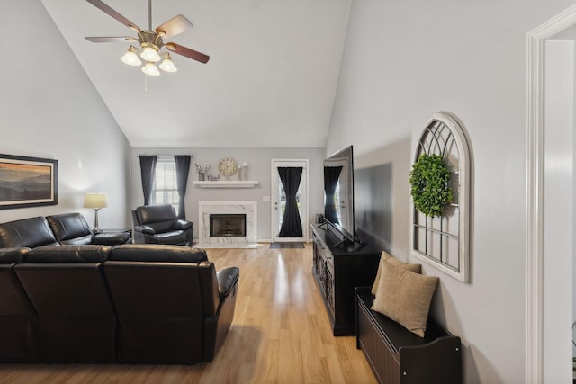 living room with ceiling fan, a premium fireplace, high vaulted ceiling, and light wood-type flooring