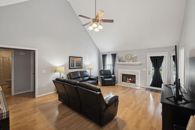 living room with ceiling fan, high vaulted ceiling, a high end fireplace, and light wood-type flooring