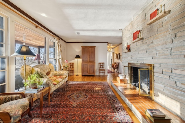 living room featuring crown molding, a fireplace, a textured ceiling, and light hardwood / wood-style floors