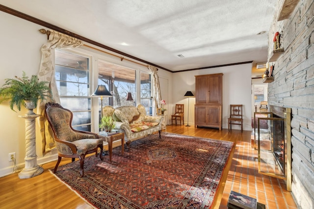 sitting room with crown molding, a stone fireplace, a textured ceiling, and light wood-type flooring