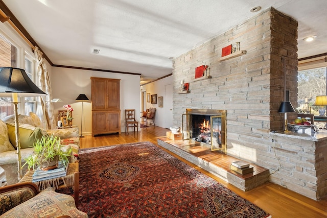 living room with ornamental molding, a stone fireplace, light hardwood / wood-style floors, and a textured ceiling