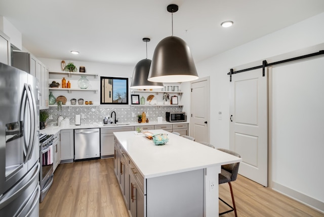 kitchen with pendant lighting, sink, stainless steel appliances, a center island, and a barn door