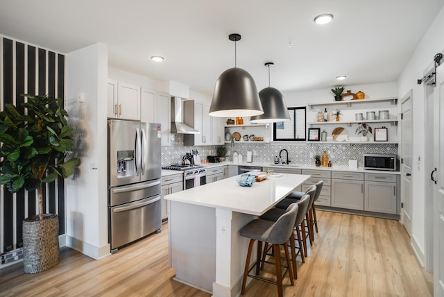 kitchen featuring appliances with stainless steel finishes, hanging light fixtures, a center island, a barn door, and wall chimney range hood