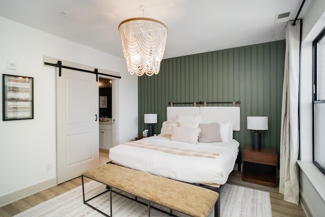 bedroom with a notable chandelier, light hardwood / wood-style flooring, and a barn door