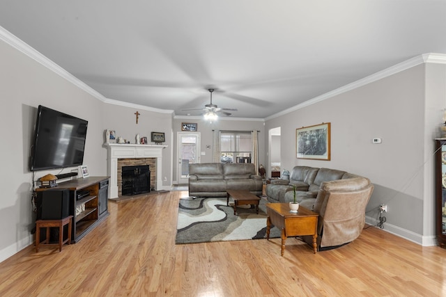 living room with crown molding, a stone fireplace, ceiling fan, and light hardwood / wood-style flooring