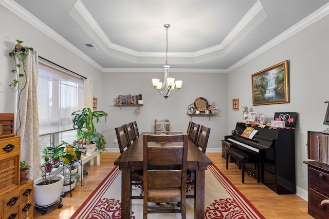 dining space with ornamental molding, light hardwood / wood-style floors, a raised ceiling, and a chandelier