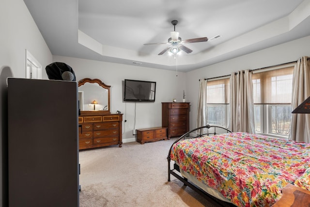 bedroom with light colored carpet, ceiling fan, and a tray ceiling